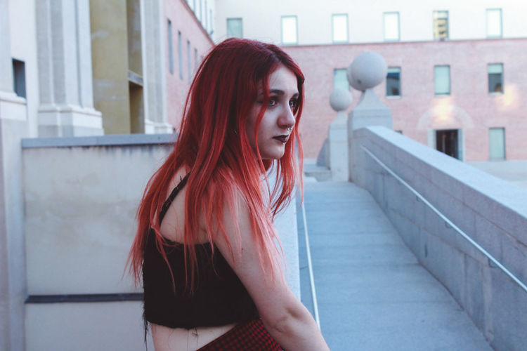 Side view of woman with red hair sitting against building