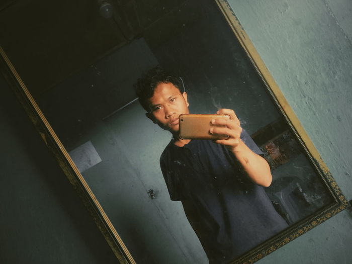 Portrait of man taking selfie in front of mirror