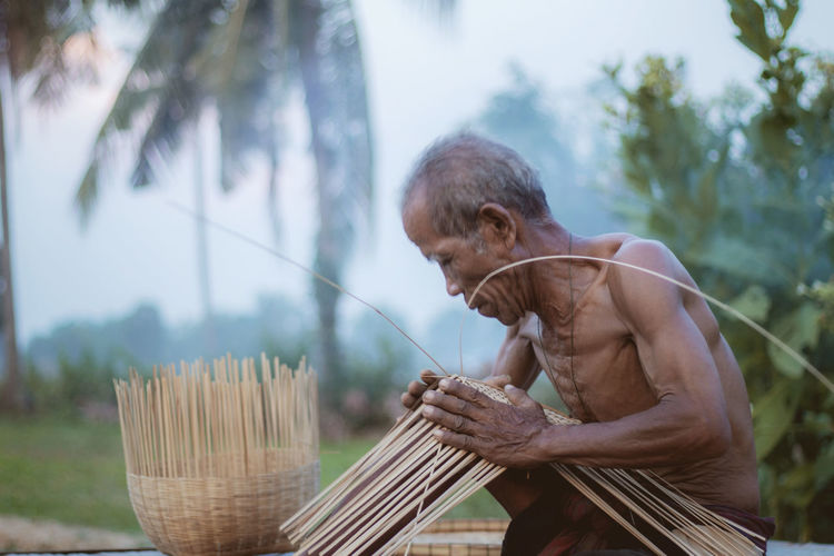 Old man are weaving in the countryside on field.