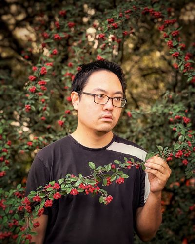 Portrait of young man holding rowan berry branch against rowan trees in the woods.
