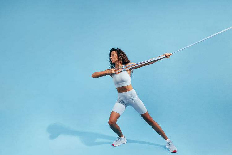 Female athlete exercising with resistance band against blue background