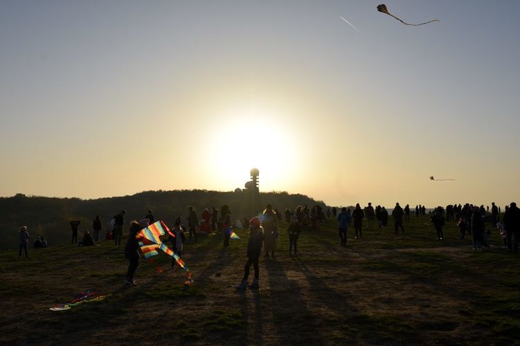 People flying kites on field against sky during sunset
