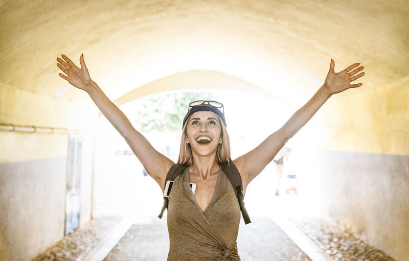 Smiling young woman with arms raised standing in tunnel