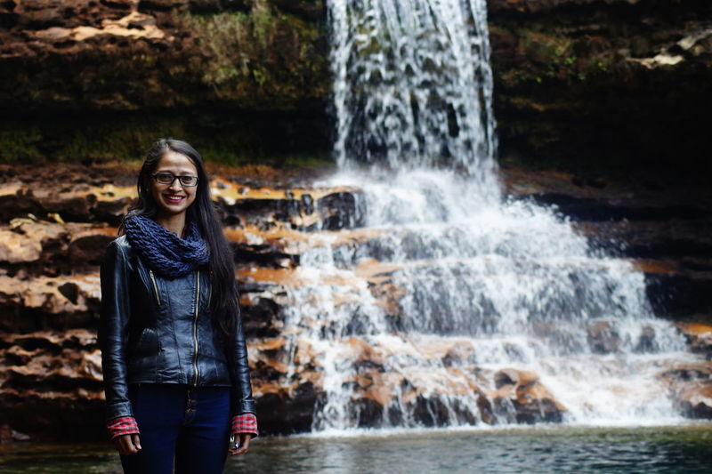 Portrait of smiling woman standing against waterfall in forest