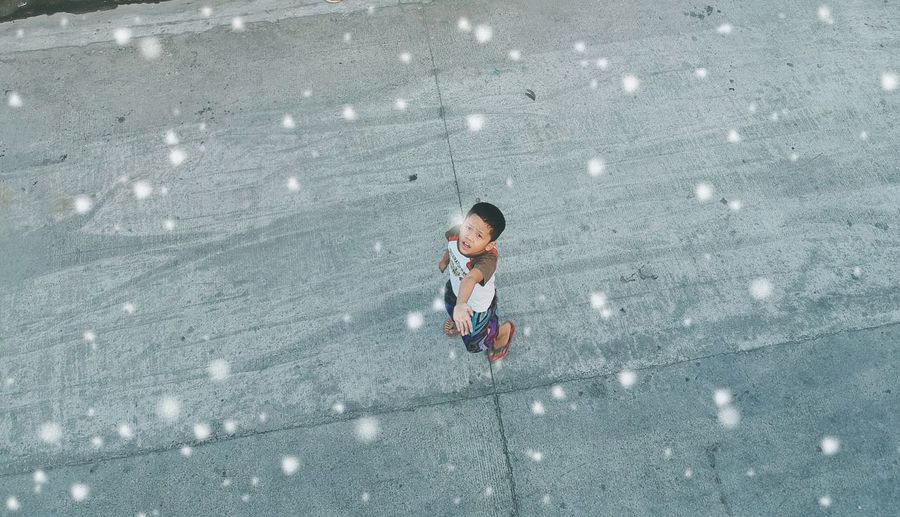 High angle view of boy standing on road during snowfall