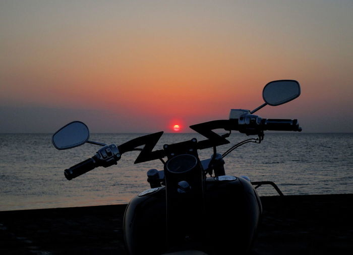 Motorcycle by sea against sky during sunset
