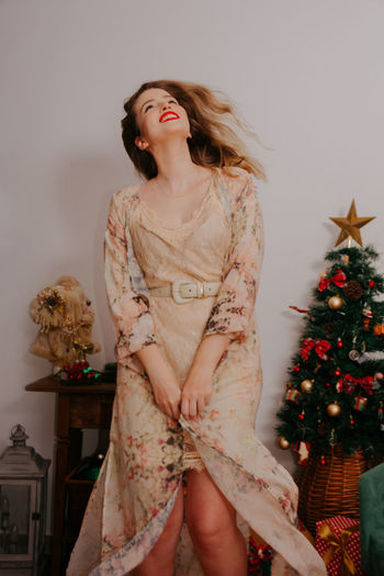 Young woman standing by christmas tree at home