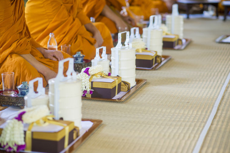 Midsection of monks sitting by gifts and lunch boxes on carpet during wedding