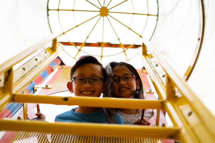 Low angle portrait of smiling siblings on outdoor play equipment