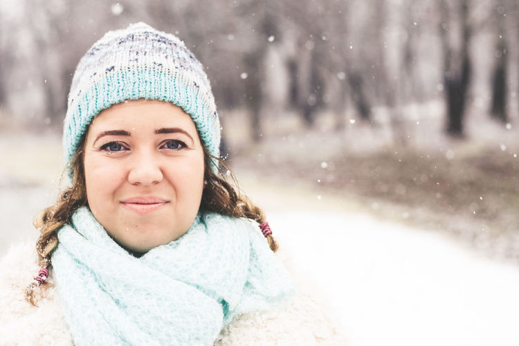 Portrait of smiling young woman standing at park during winter