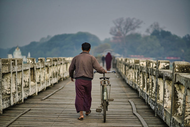 Rear view of man walking with bicycle on footpath