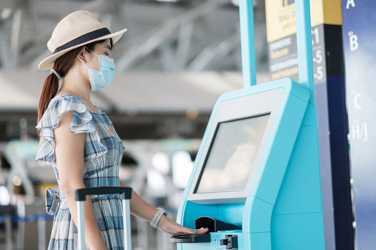 Side view of woman wearing mask using atm at airport