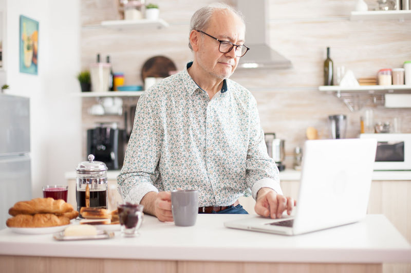 Senior man holding coffee cup while using laptop