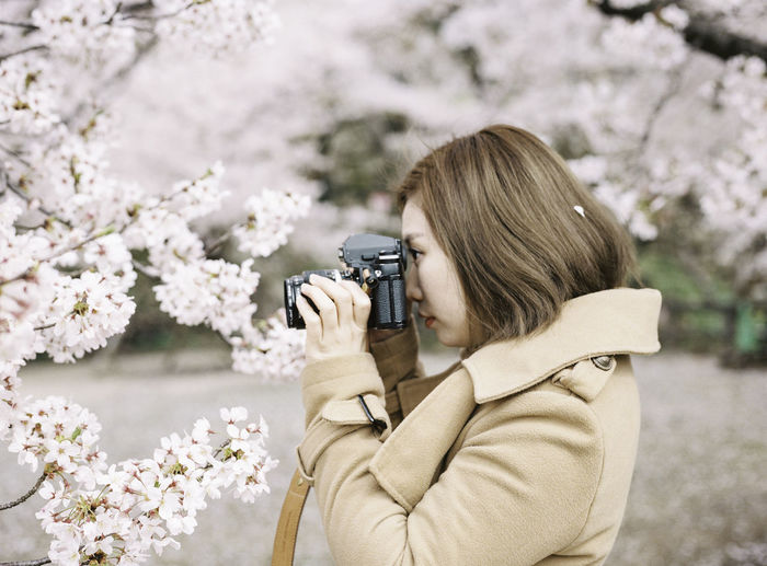 Side view of young woman photographing flowers