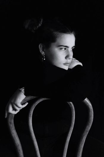 Lonely beautiful woman sitting on chair against black background