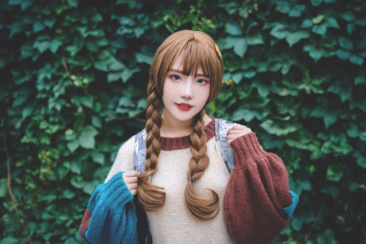 Portrait of young woman with braided hair standing against plants at park