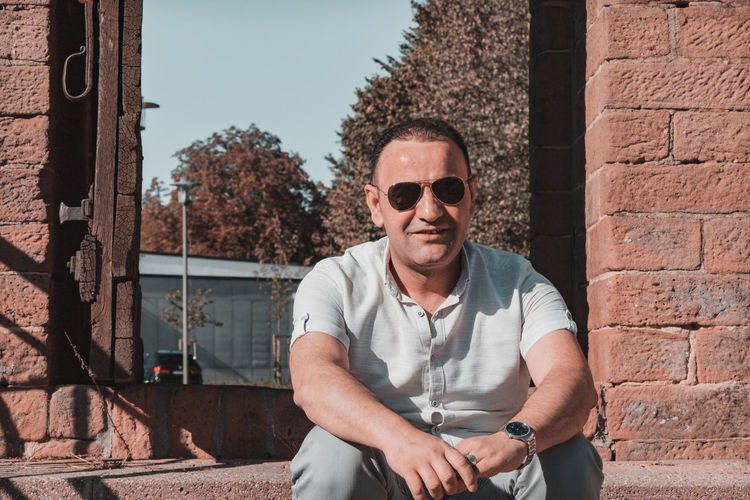 Portrait of man wearing sunglasses standing against brick wall
