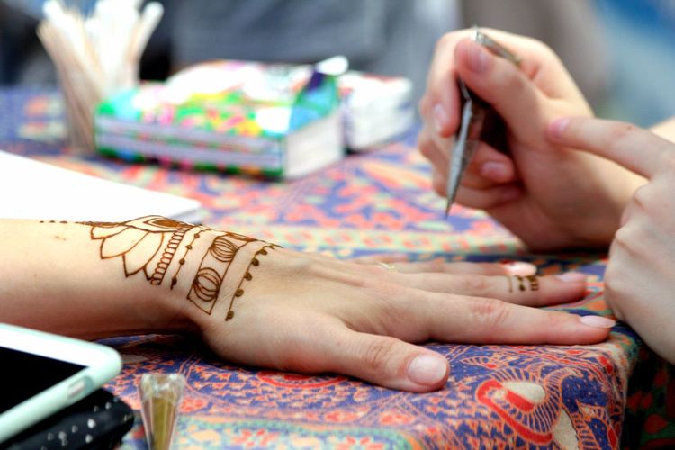 Cropped hands of woman making henna tattoo on table