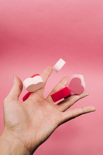 Close-up of woman hand holding heart shape over pink background