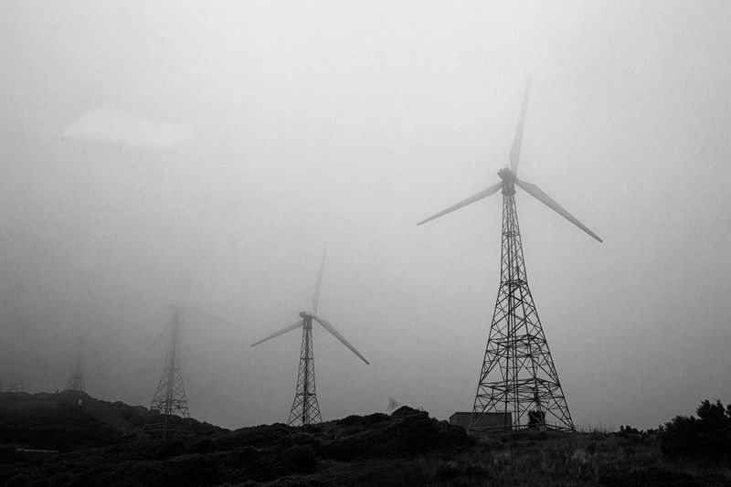 Windmills on field against sky during foggy weather