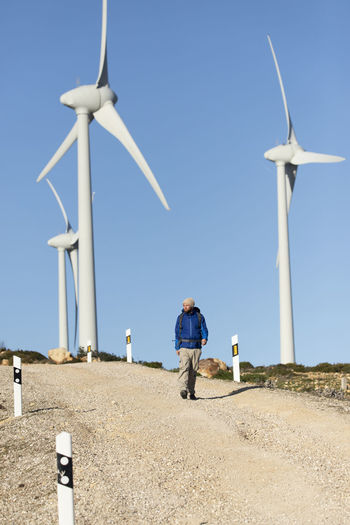 Spain, andalusia, tarifa, man on a hiking trip walking on dirt road surrounded by wind turbines