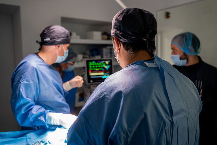 Surgeons and nurses in uniform concentrating and operating patient using special equipment in operating room of contemporary hospital