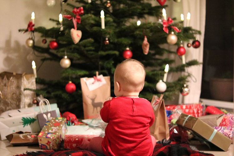 Rear view of baby sitting by gifts against christmas tree at home