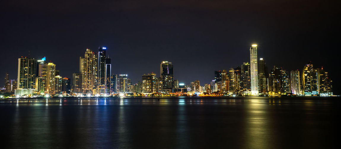 Illuminated buildings by sea against sky at night, skyline of panama