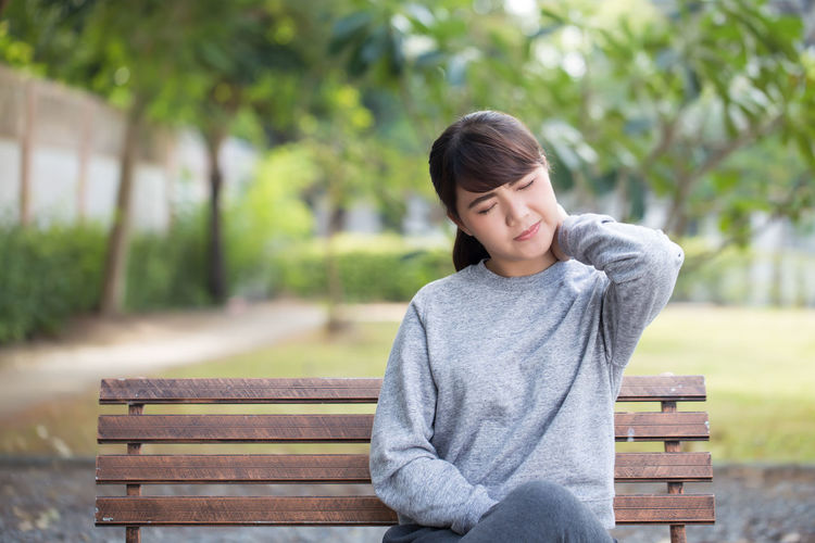 Young woman with neck pain sitting on park bench