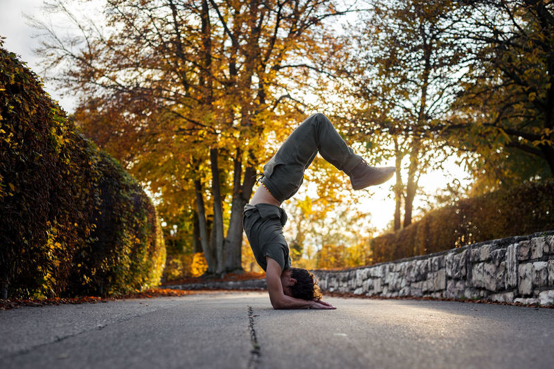 Side view of man doing handstand on road during autumn