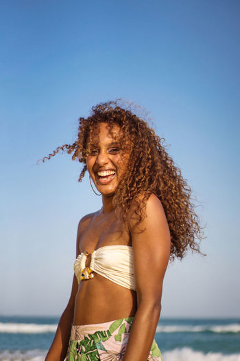 Low angle portrait of young woman with dark skin and long curly hair at the beach