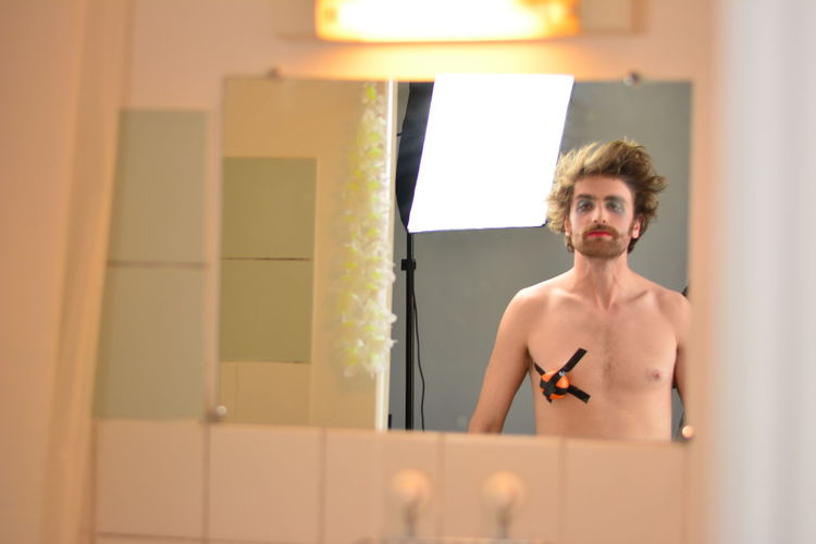 Portrait of shirtless man with face paint and duct tape on chest in bathroom