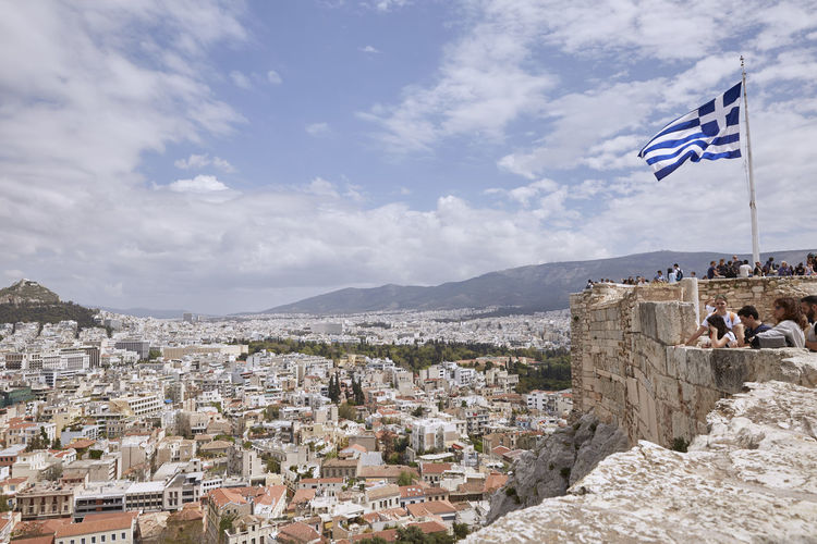 People with greek flag at acropolis of athens looking at townscape against sky
