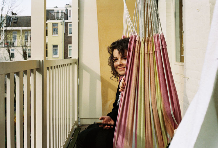Portrait of smiling woman sitting in hammock at balcony