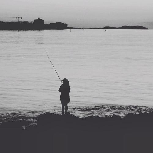 Man fishing in sea at sunset