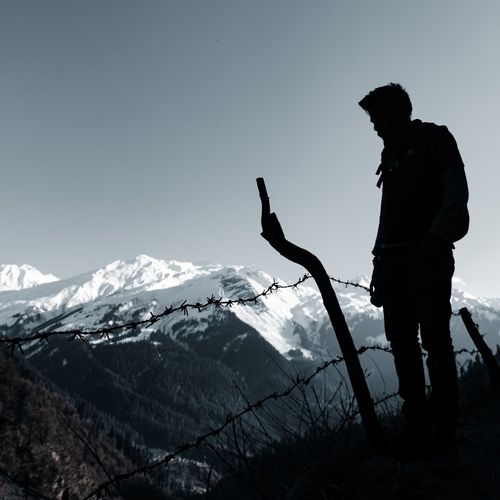 Silhouette man standing on snowcapped mountain against sky