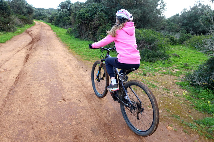 Girl in pink jumper riding a mountain bike along a dirt track