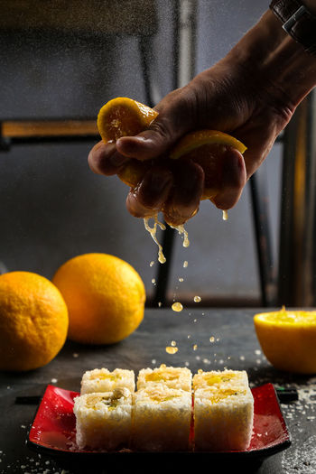 Cropped image of hand crushing orange fruit on sushi in plate