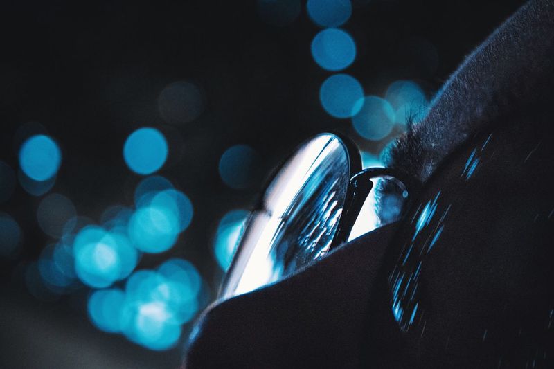 Cropped image of woman wearing eyeglasses against blue lens flare at night