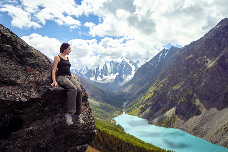 Full length of woman sitting sitting on cliff against mountain