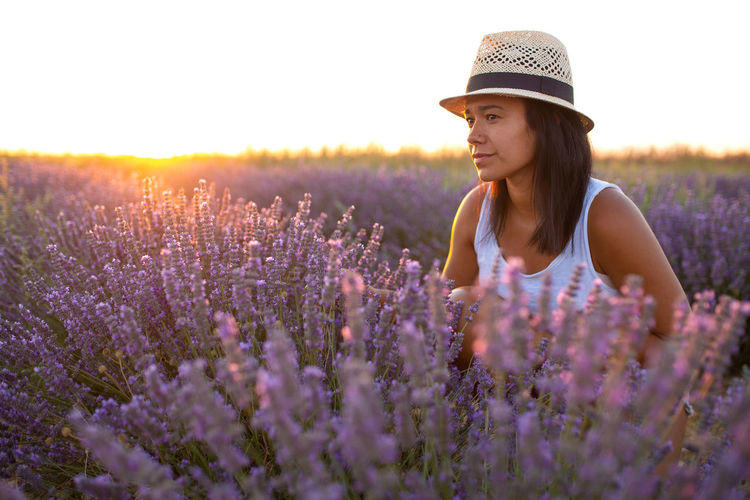 Young woman with hat is pensive in lavender flowers at sunset