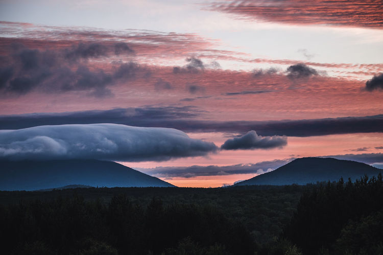 Vibrant red and pink sunset and clouds over distant mountains in maine