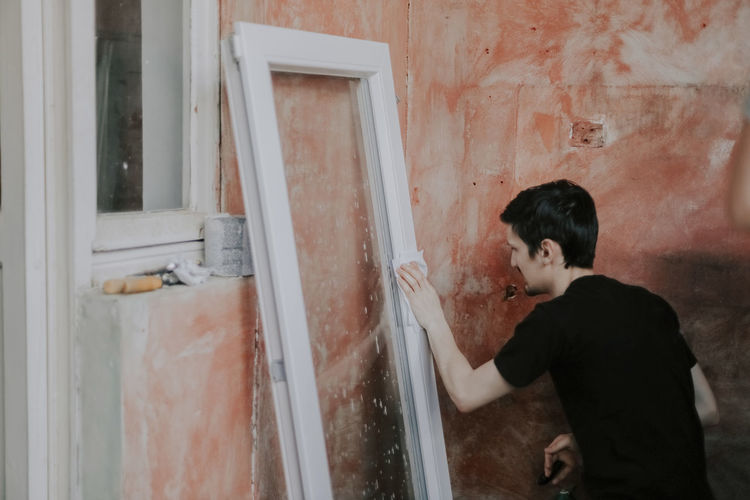 Caucasian young man wipes a window frame with a dry paper napkin.