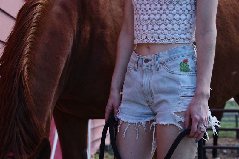 Midsection of young woman standing by horse at barn