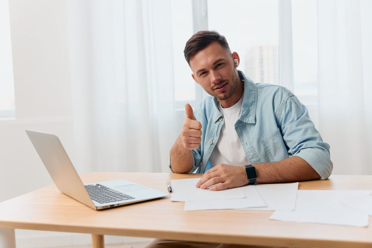 Portrait of smiling business man showing thumbs up gesture sitting at table