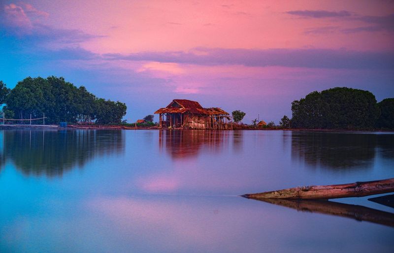 Scenic view of lake by building against sky during sunset