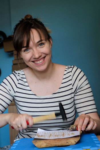 Portrait of smiling young woman hammering nails on table at home