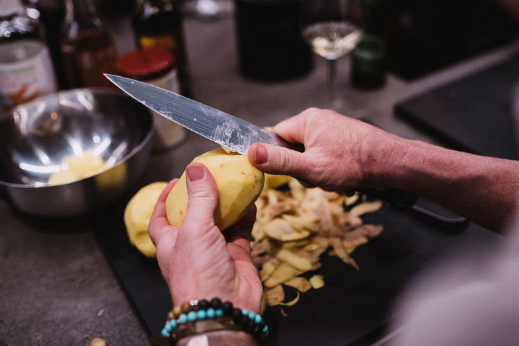 From above anonymous person with bracelet using sharp knife to peel fresh potato over in kitchen during cooking lesson in navarre, spain person