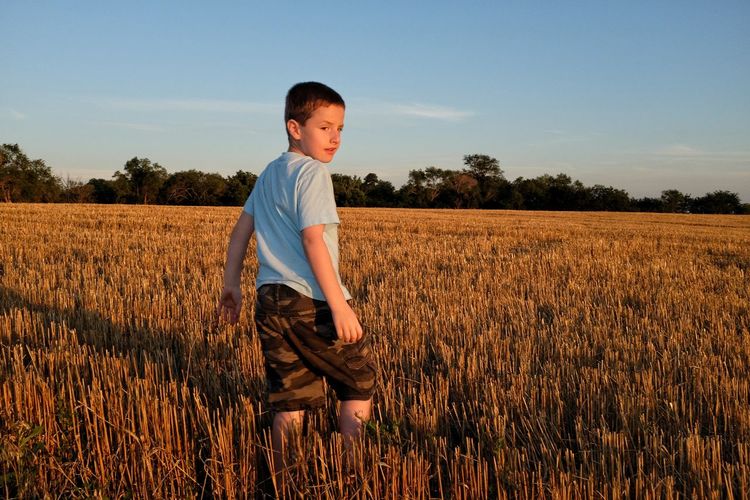Boy standing on field stubble during sunset