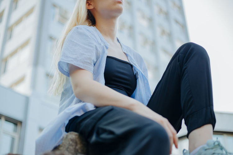 Low angle view of young woman sitting against building